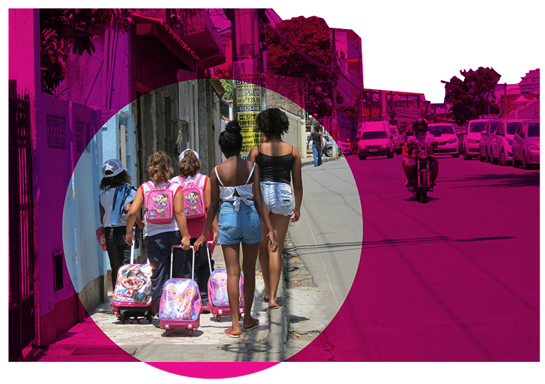 A imagem é uma foto de uma rua da Comunidade da Polêmica mostrando cinco crianças andando, de costas para a foto, com uniforme da escola numa calçada estreita. Destacamos com um círculo rosa esses pedestres em contraste com o restante do espaço da rua, resrervado para os carros.